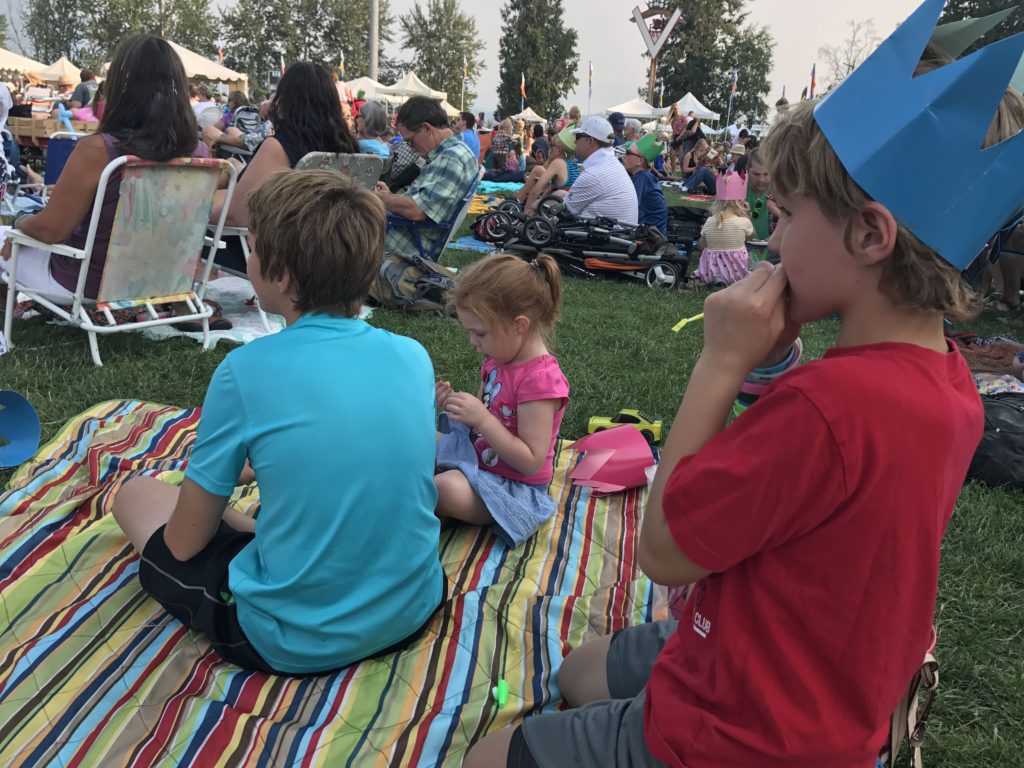 3 kids sitting on a blanket watching the show at the festival at sandpoint
