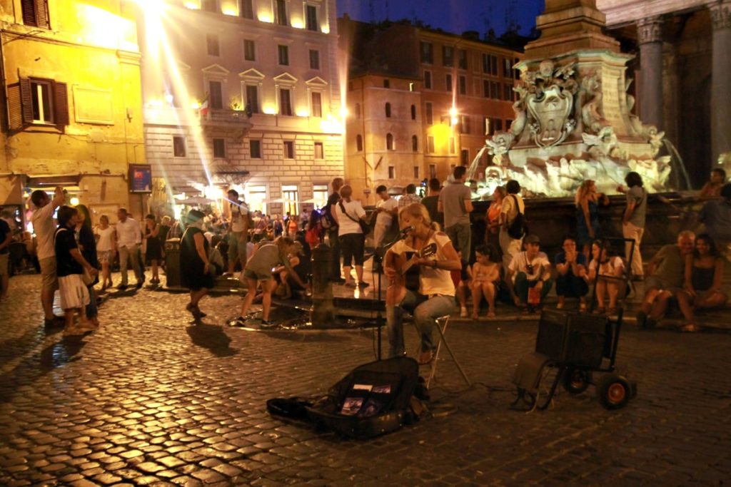 Woman playing guitar for a crowd at Piazza della Rotondo in Rome at night.