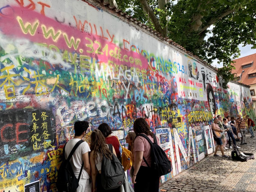 John Lennon wall in Prague. Wall filled with graffiti, people writing on wall.
