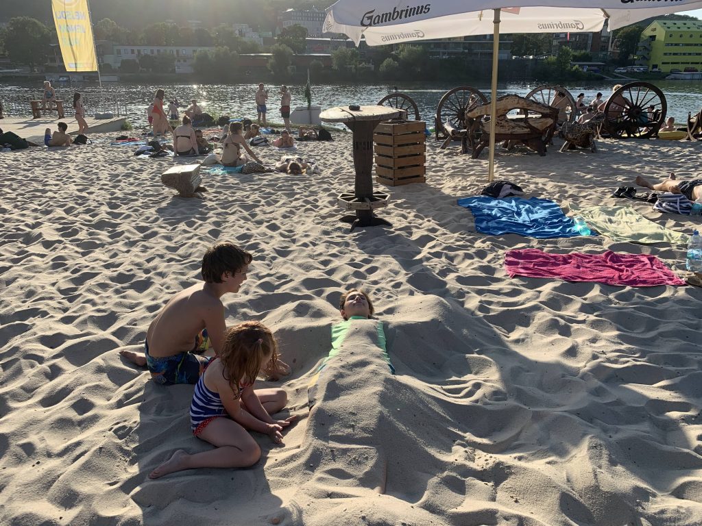 kids playing in the sand at the zlute lazne beach in prague with river in the background