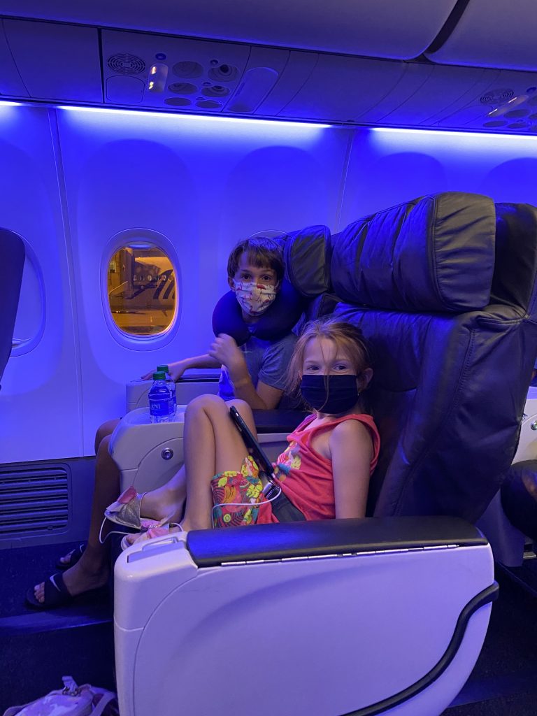 two kids wearing masks in first class on an airplace traveling during a pandemic